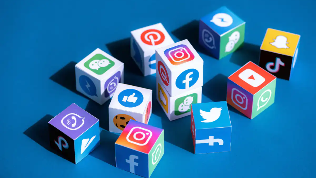 Social Media Kanäle in Form von diversen Würfeln mit den Logos der jeweiligen Plattformen drauf, blauer Boden als Hintergrund